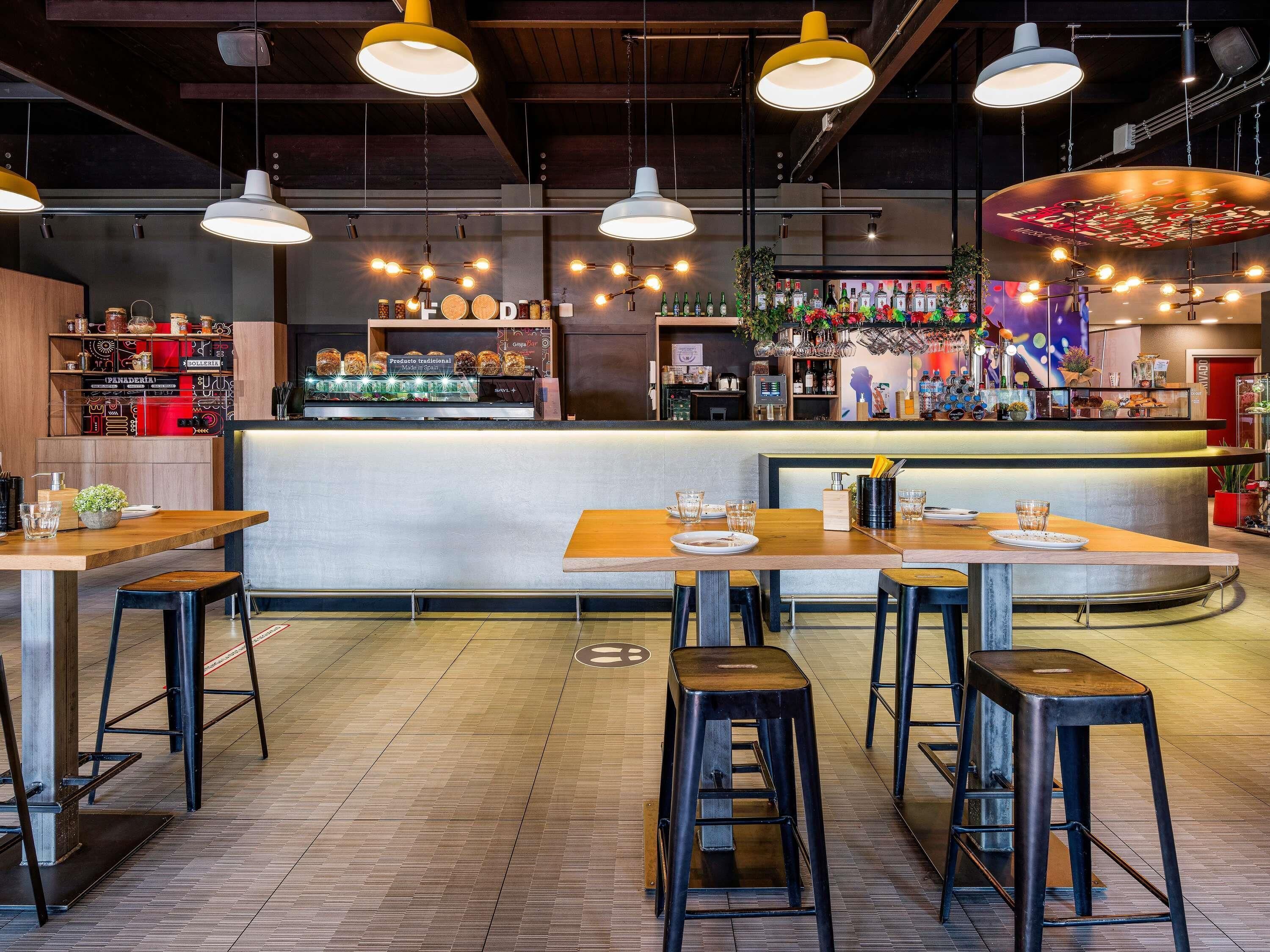 Zona de bar con taburetes, una barra y estantes con botellas.
