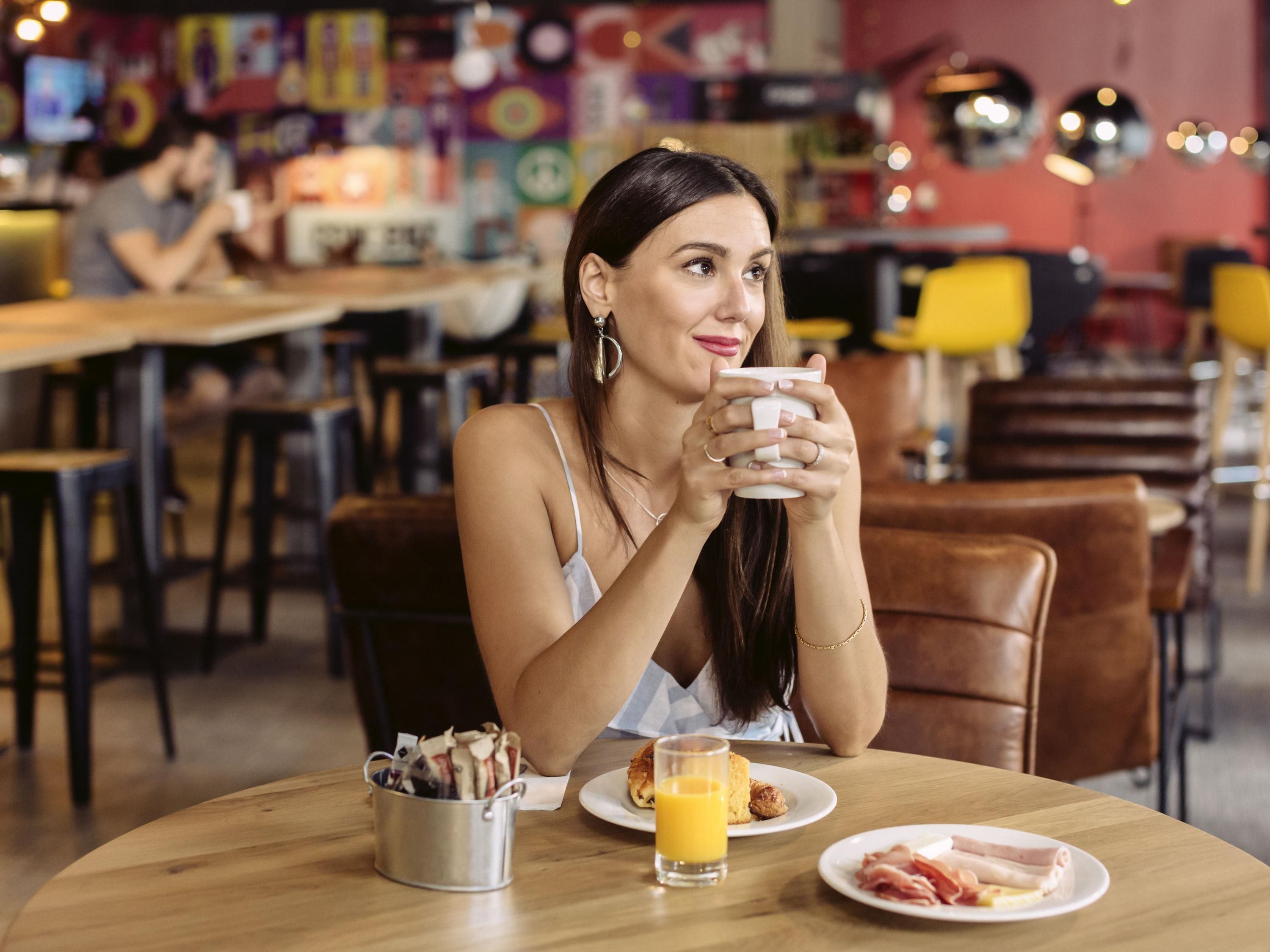 Una persona sentada a una mesa con alimentos para el desayuno, como huevos y tocino, en un café con sillas y mesas.