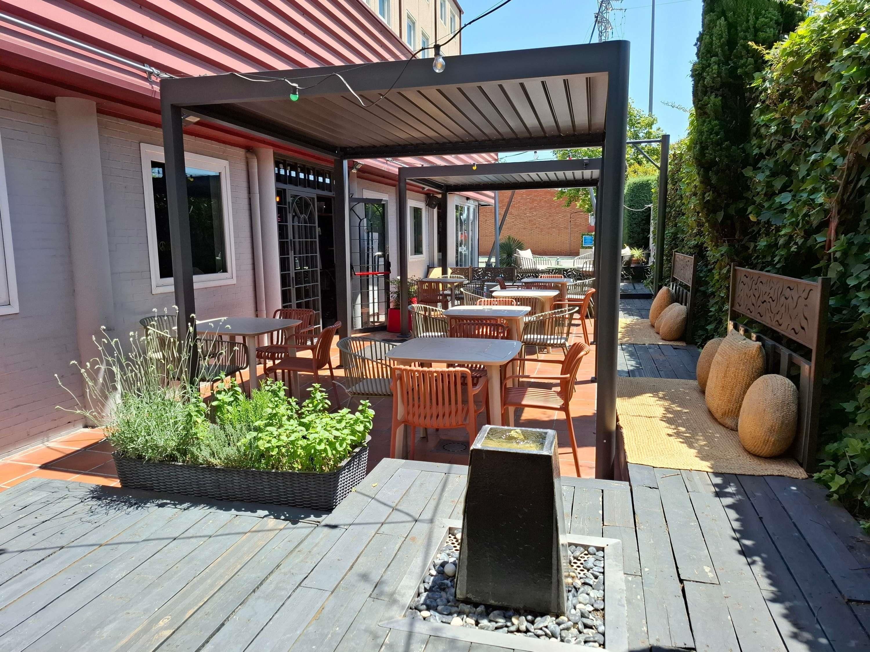 An outdoor patio area with tables and chairs, a planter with greenery, and a water feature.