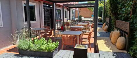 An outdoor patio area with tables and chairs, a planter with greenery, and a water feature.
