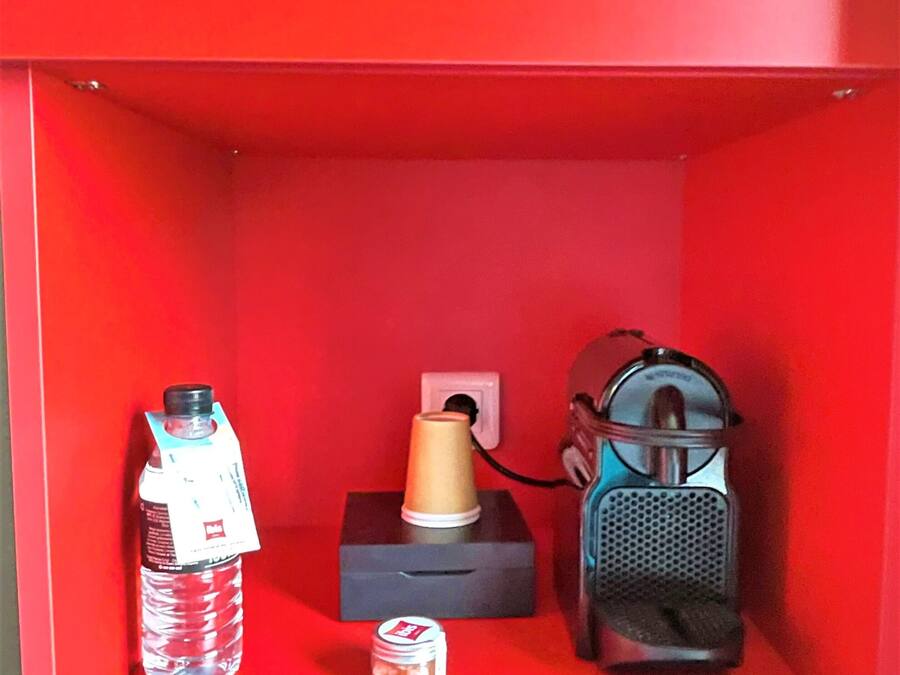 Una estantería roja con una botella de agua, un frasco pequeño y un altavoz portátil.