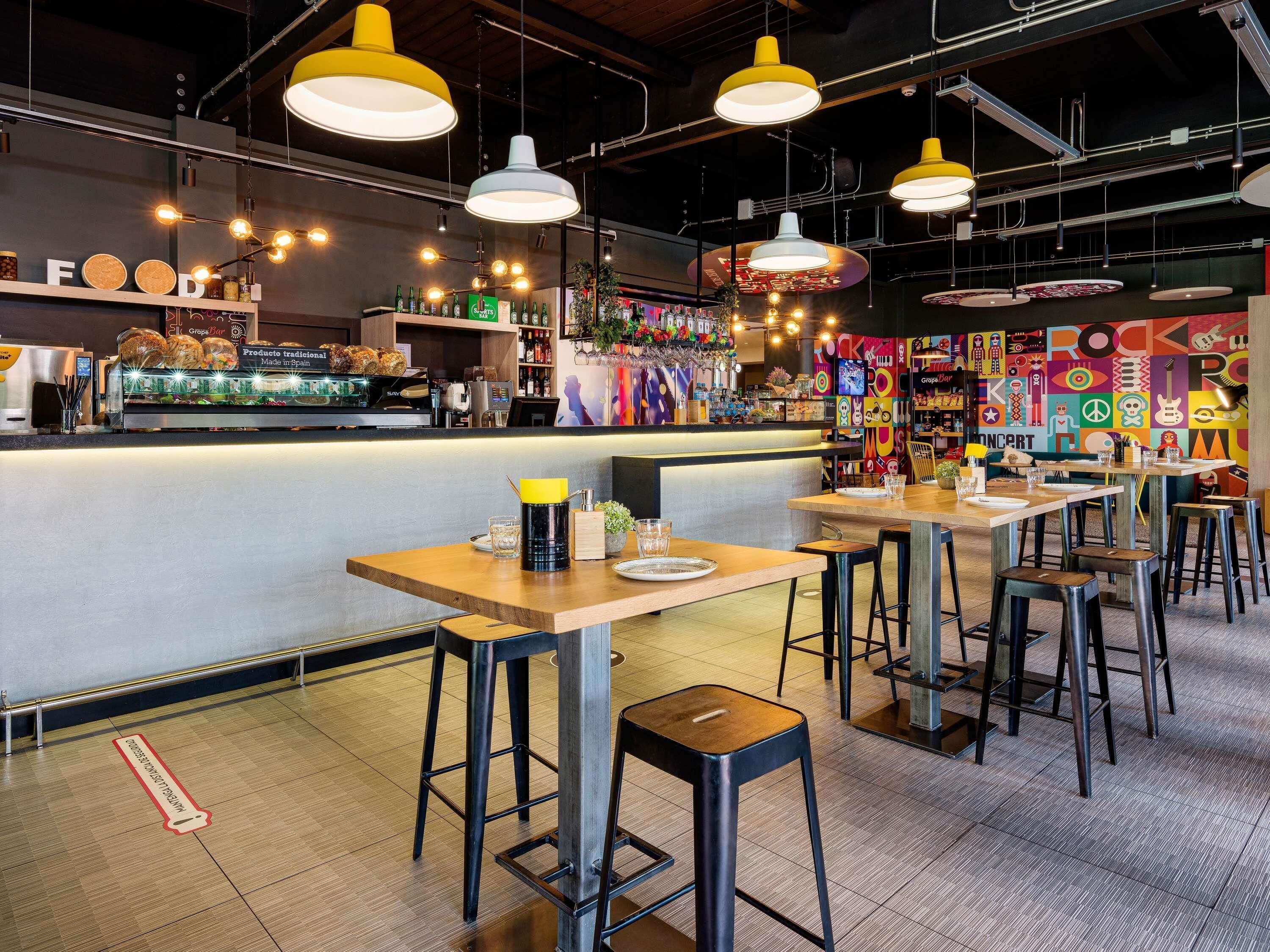 A restaurant interior with multiple tables, bar area, and a colorful mural on the wall.