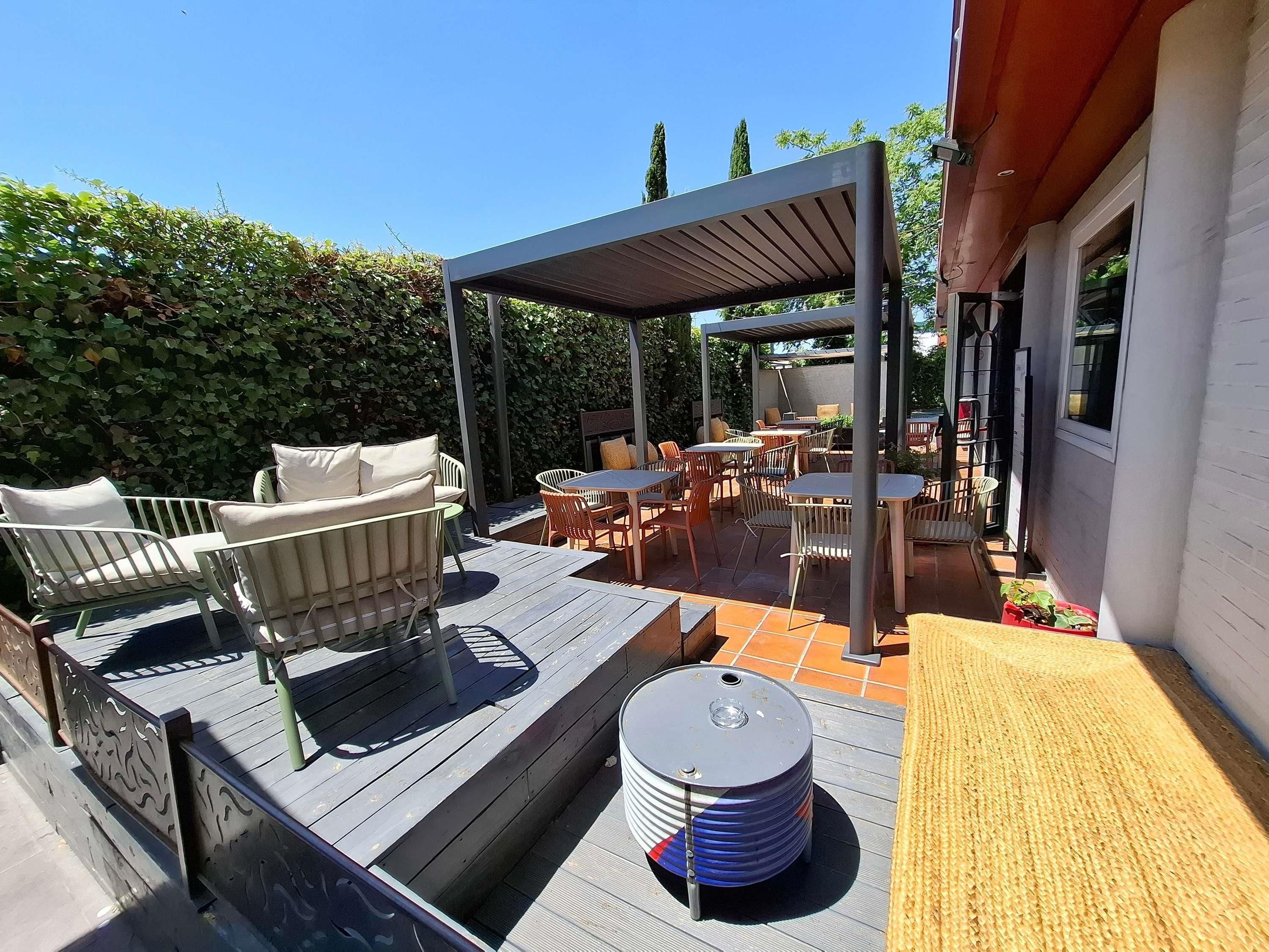 Zona de pati exterior amb una pèrgola, seients i una taula petita.