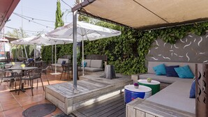 Un patio al aire libre con mobiliario de madera, sombrillas y una zona de estar con cojines y una pequeña mesa.