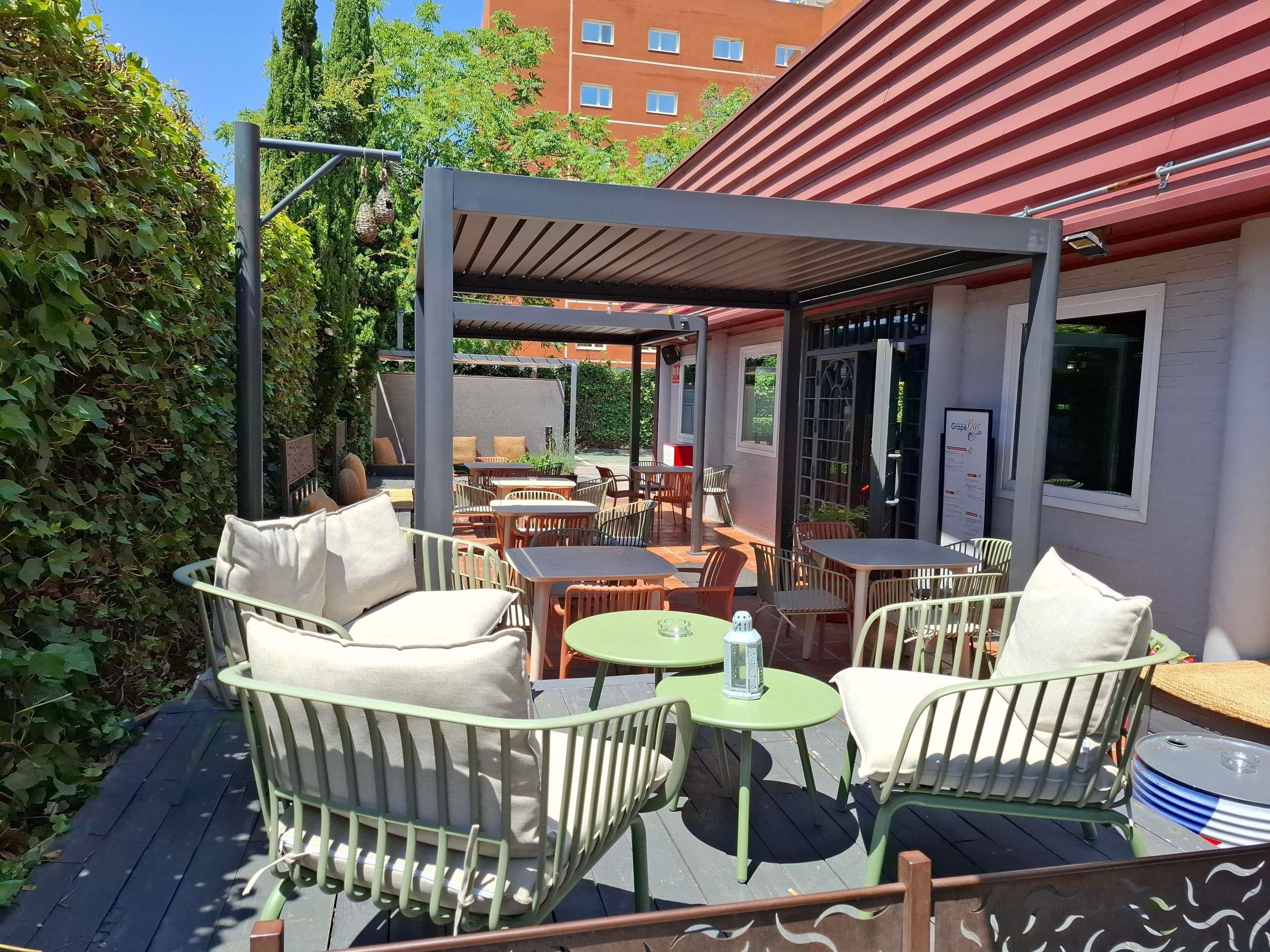 An outdoor seating area with tables and chairs, a covered section, and a building in the background.