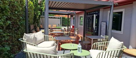 An outdoor seating area with tables and chairs, a covered section, and a building in the background.