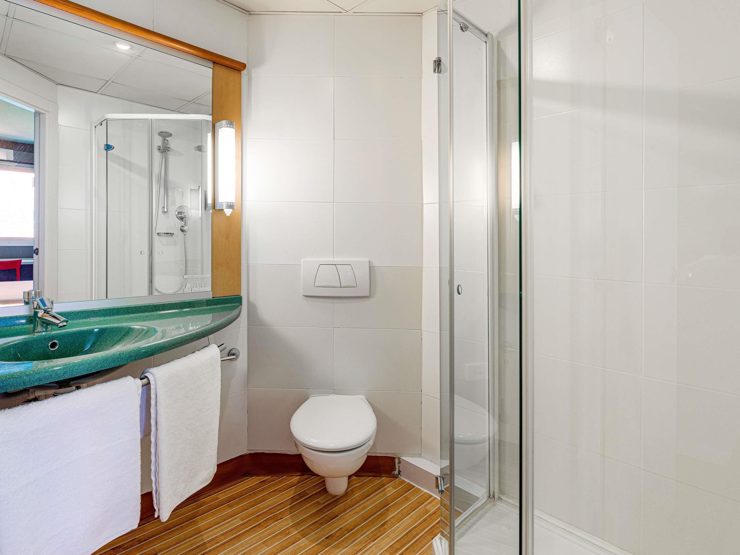 A bathroom with a glass shower enclosure, a white toilet, and a green marble sink.