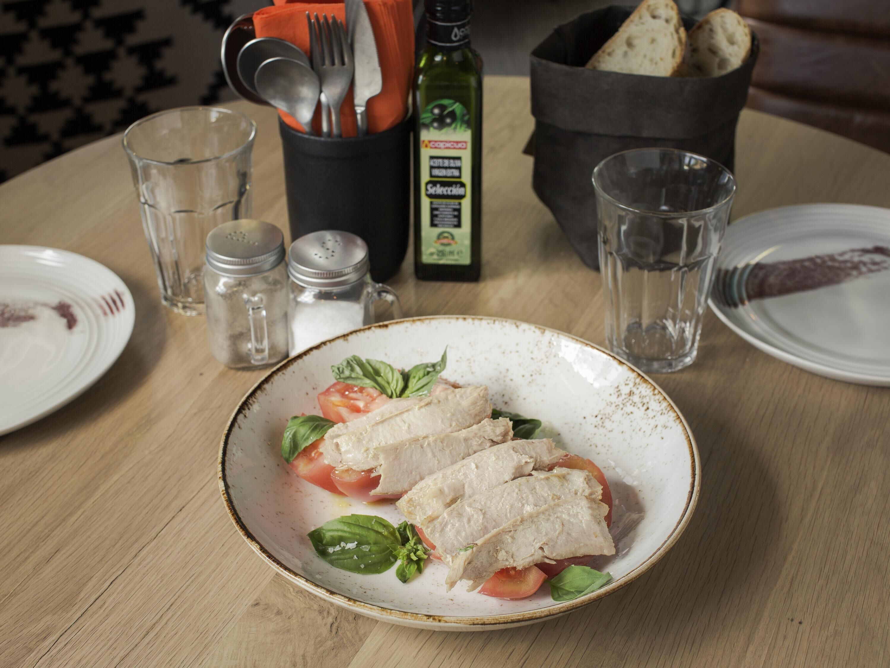 A plate of fish with tomatoes and basil on a wooden table.