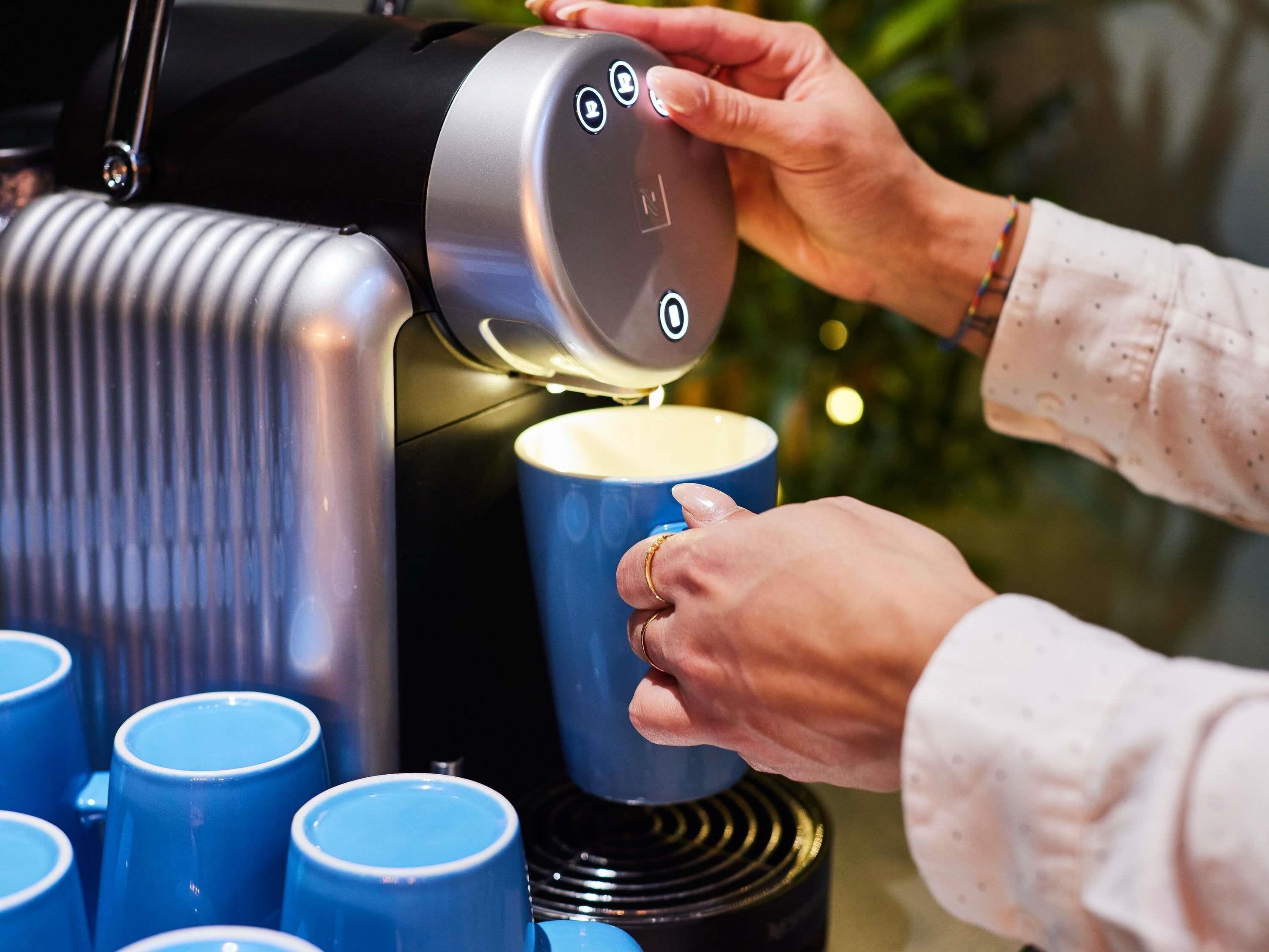 A person operating a coffee machine, dispensing coffee into a blue cup.