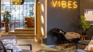A modern interior with a neon sign reading 'GOOD VIBES,' a bar sign, and a seating area with a plant and a fluffy chair. - Novotel Edinburgh Centre (Edinburgh)