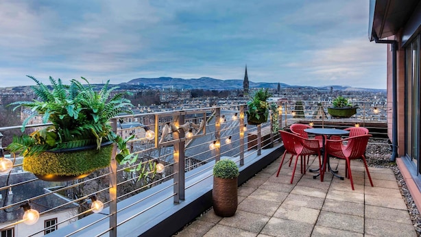 A rooftop terrace with potted plants, red chairs, and a view of a cityscape. - Novotel Edinburgh Centre (Edinburgh)