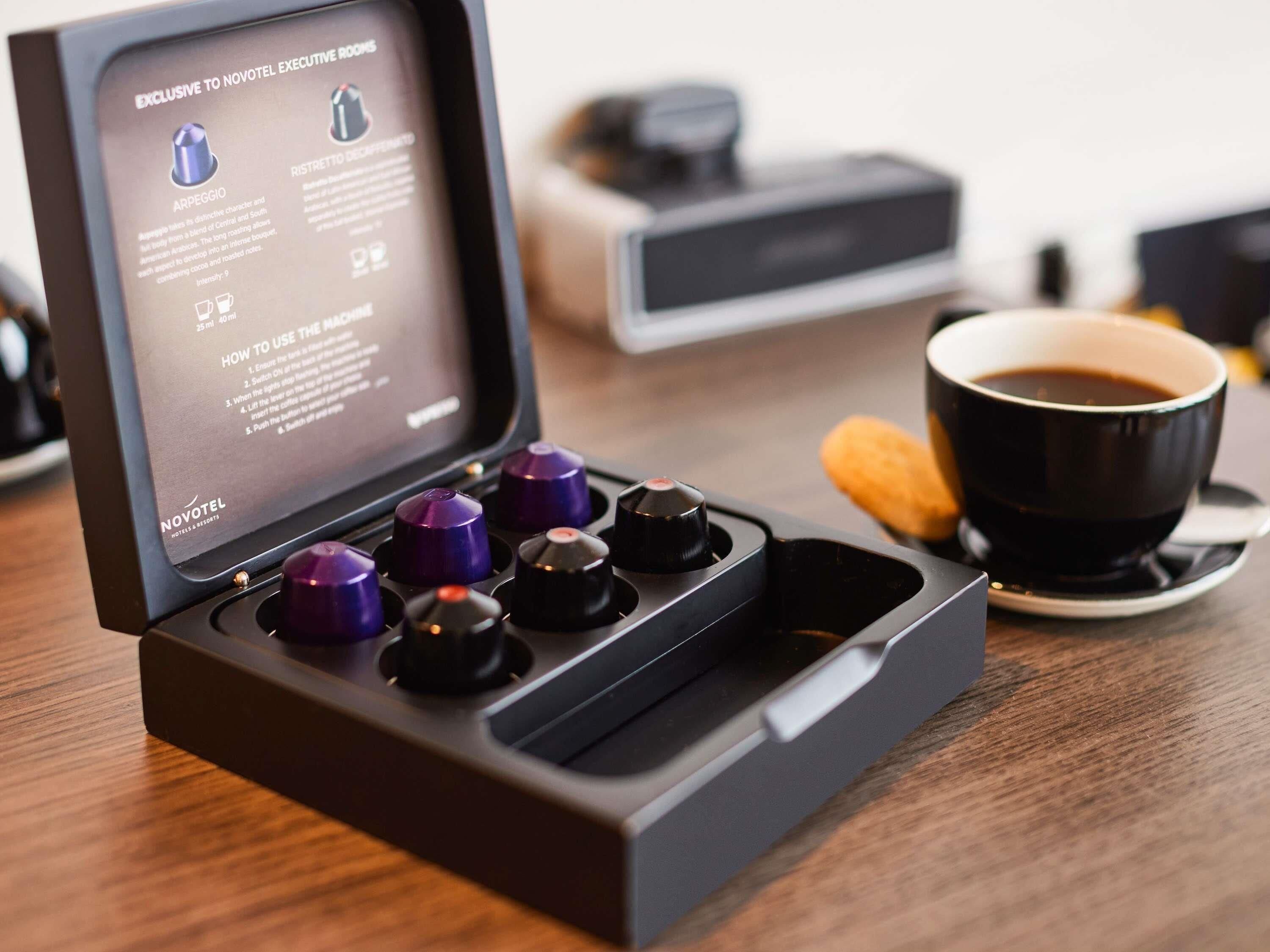 Une machine à café accompagnée de son manuel d’utilisation, une tasse de café et une pâtisserie sur une table.