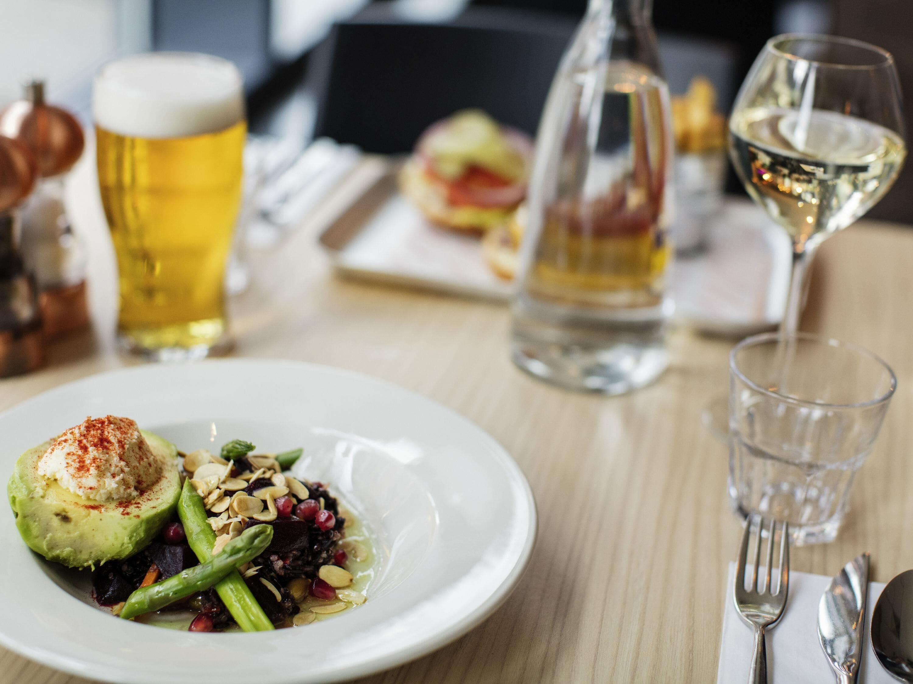 A dining table with a plate of food, a glass of beer, a bottle of wine, and a glass of water.