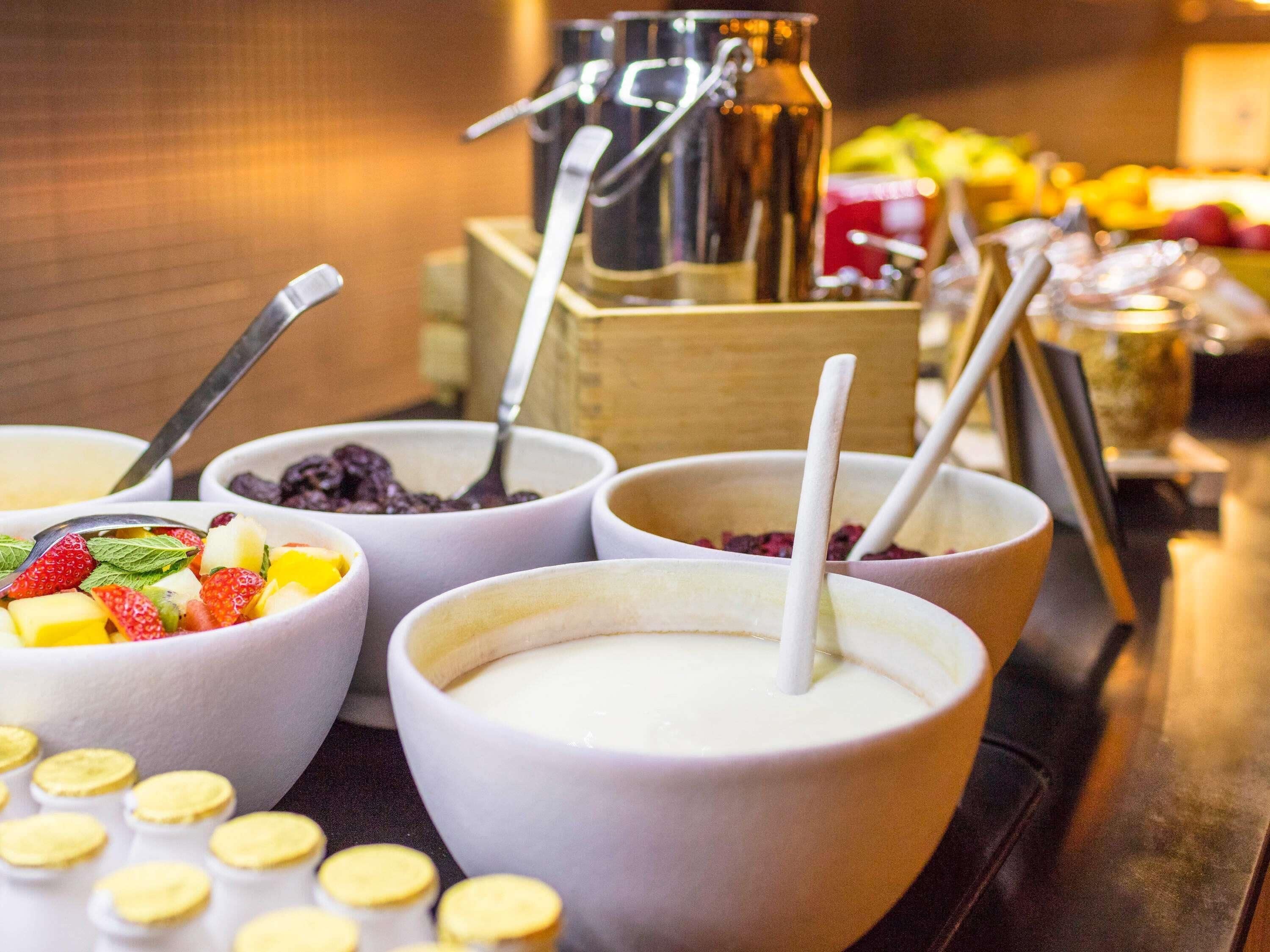 A buffet with various bowls of food and drinks, including bowls with fruits and a coffee machine in the background.