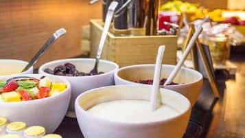A buffet with various bowls of food and drinks, including bowls with fruits and a coffee machine in the background.