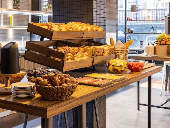 Un bufé de desayuno con diversos pasteles, frutas y una máquina de café.