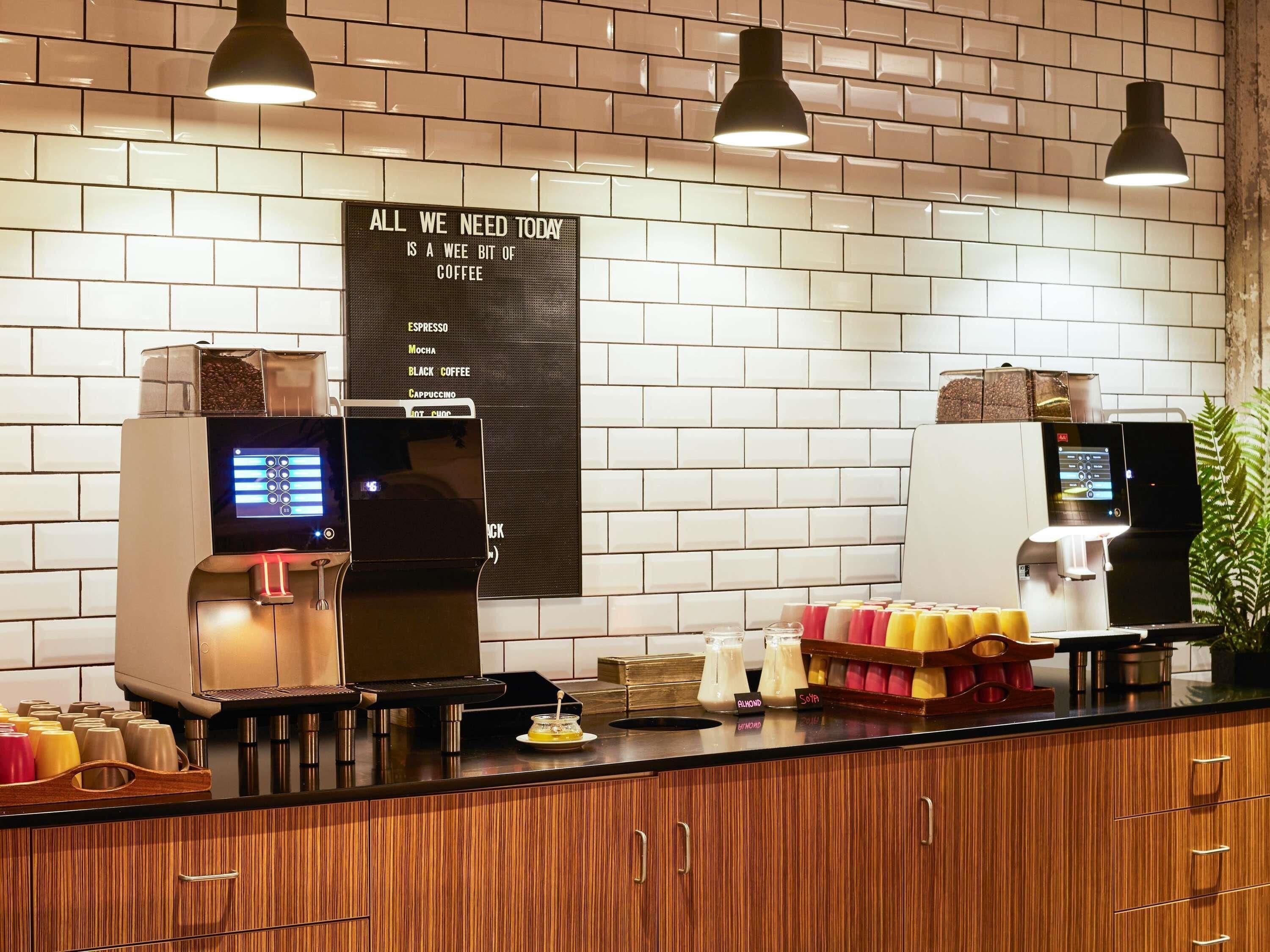 Un espace dédié au café, avec une machine  à expresso et une autre pour les cappuccinos, un tableau affichant le menu et une plante.