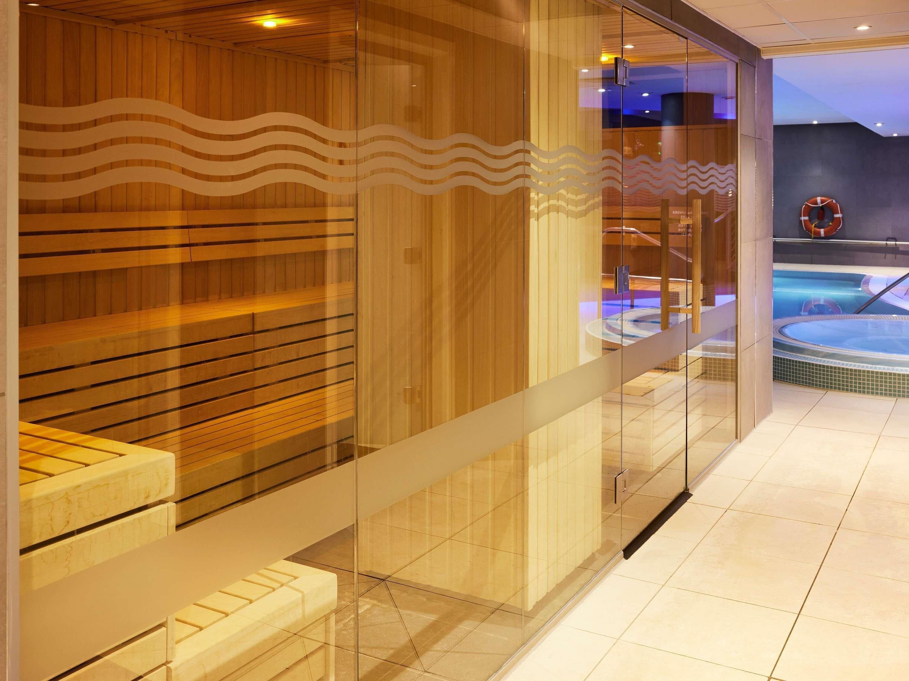 Een modern wellnessruimte met houten lambrisering en glazen deuren, een zichtbare hottub en een reddingsboei aan de muur.