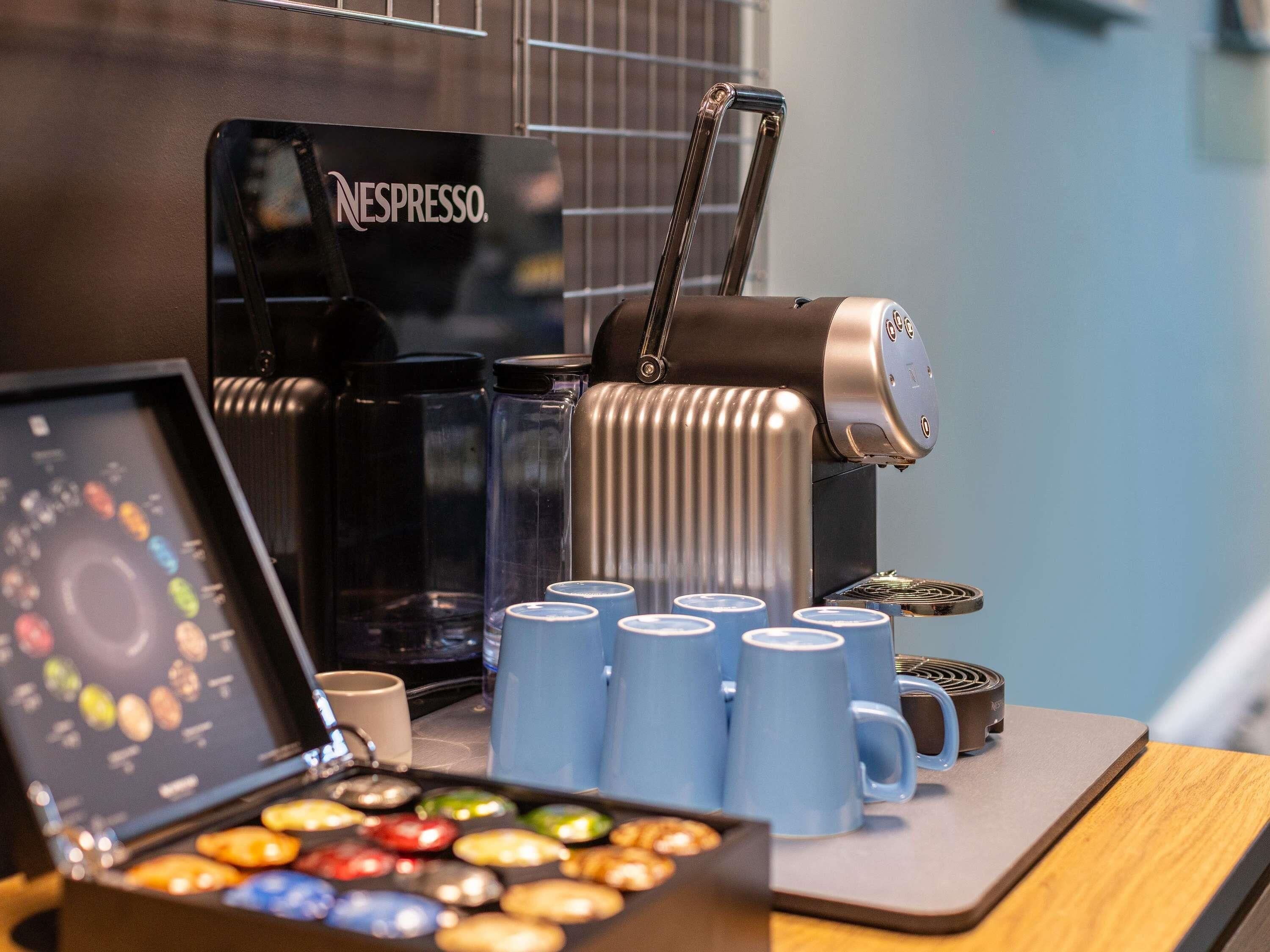 A coffee machine, a coffee cup, and a box of assorted cookies on a table.
