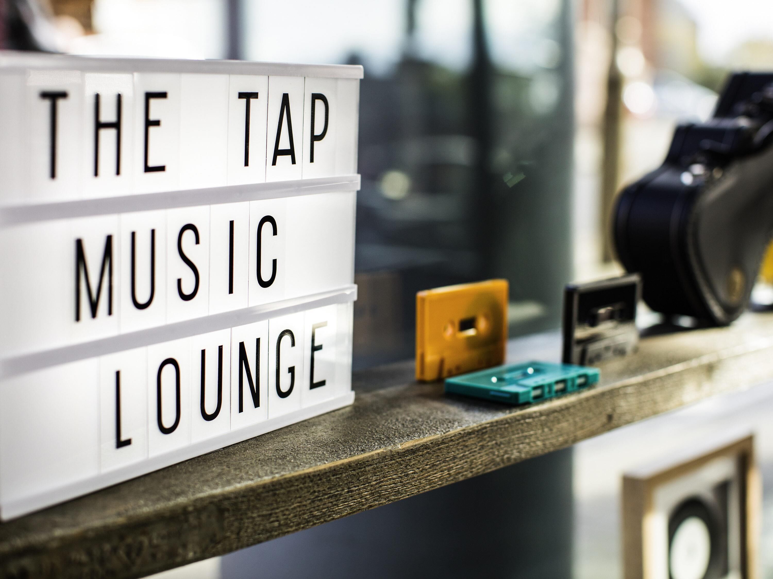 A sign with the words 'THE TAP MUSIC LOUNGE' on a wooden surface.