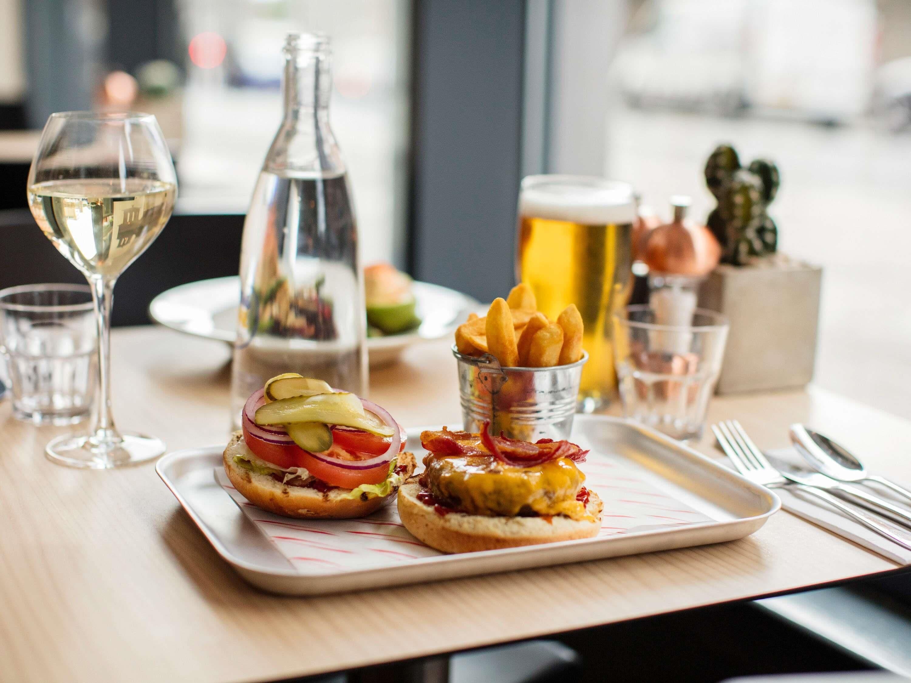 A dining table with two burgers, a glass of white wine, a beer mug, and a small cup of fries.