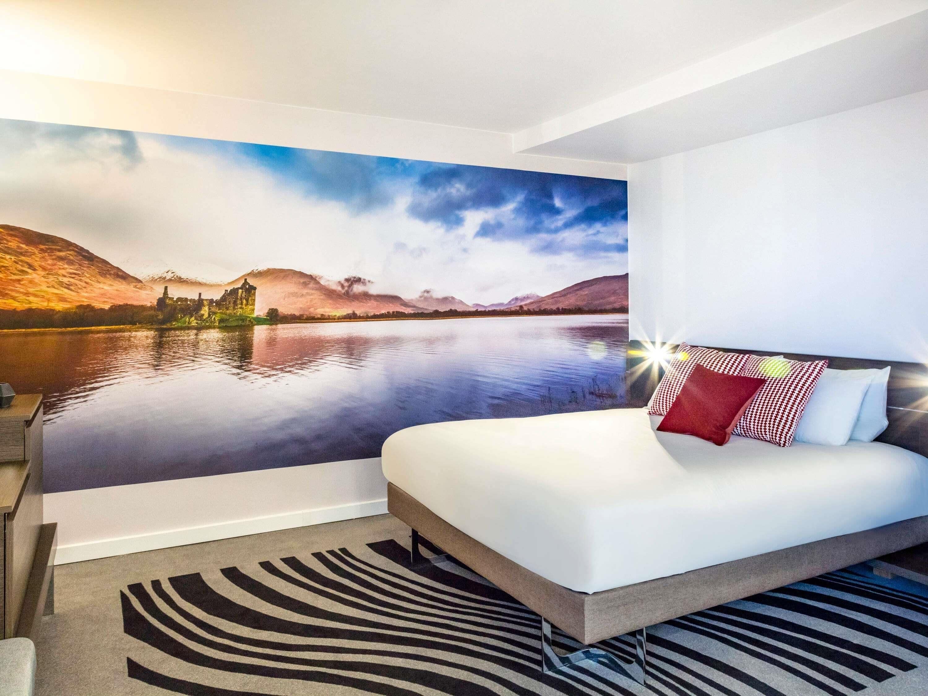 A bedroom with a bed, a zebra-patterned rug, and a scenic mural of a lake and mountains.