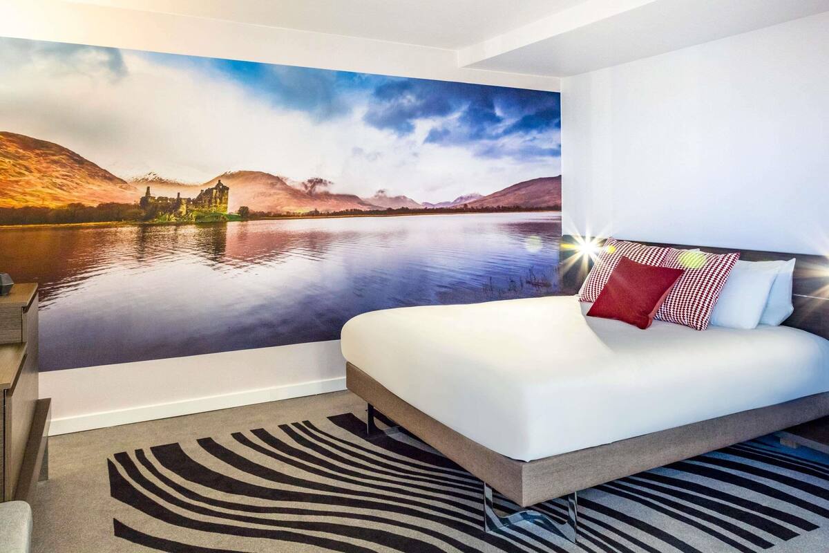 A bedroom with a bed, a zebra-patterned rug, and a scenic mural of a lake and mountains.