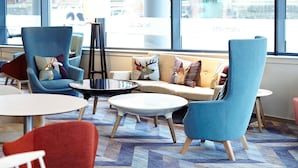 A modern lounge area with a sofa, armchairs, and a coffee table, featuring a large window with a city view. - Novotel Edinburgh Centre (Edinburgh)