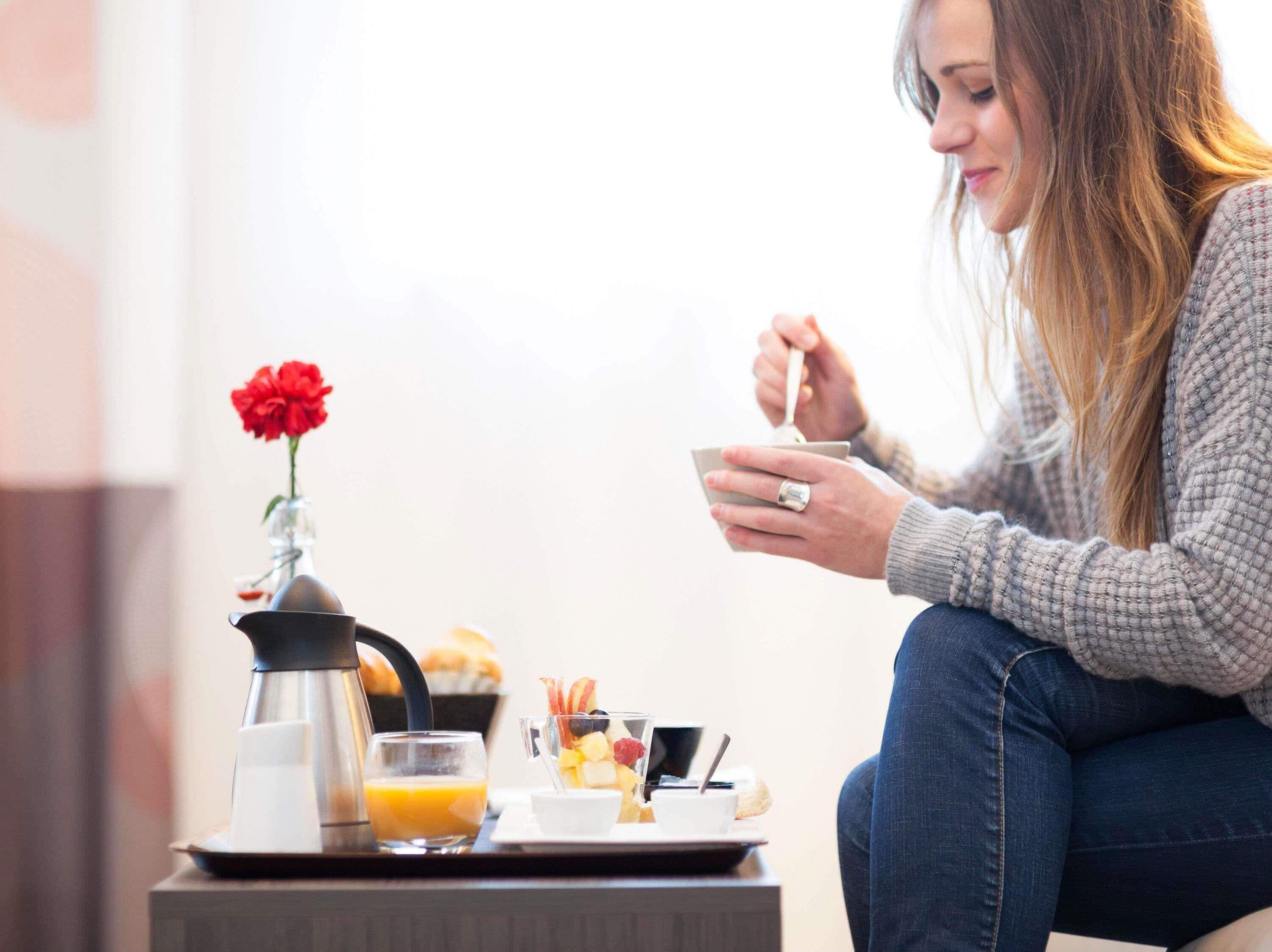 Uma mesa de pequeno-almoço com um bule de café, um copo de sumo de laranja, um prato com comida e um vaso de flores.