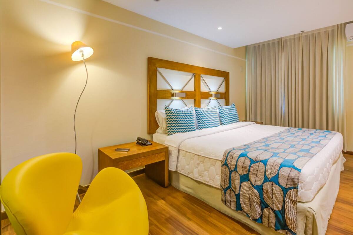 Une chambre d’hôtel avec un lit, une table de chevet, une lampe, une chaise et un rideau.