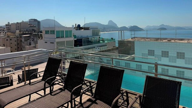 A rooftop pool with glass railings, wicker chairs, and a view of the ocean and mountains. - Rio Design Copacabana Hotel (Rio de Janeiro)