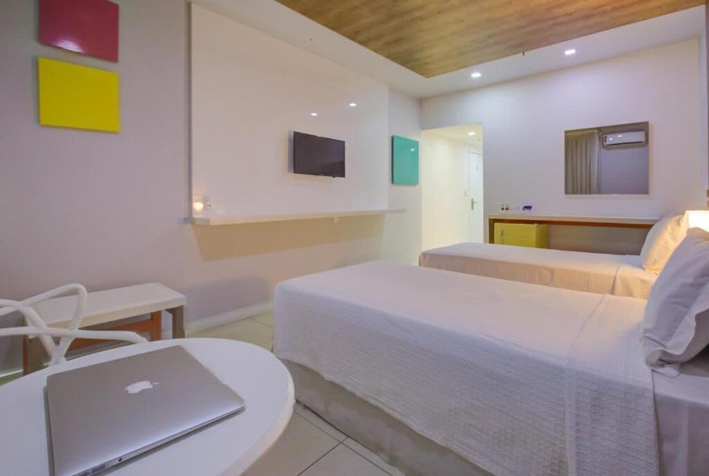 Habitación de hotel con una cama, un escritorio con una computadora portátil, un televisor y una mesita.