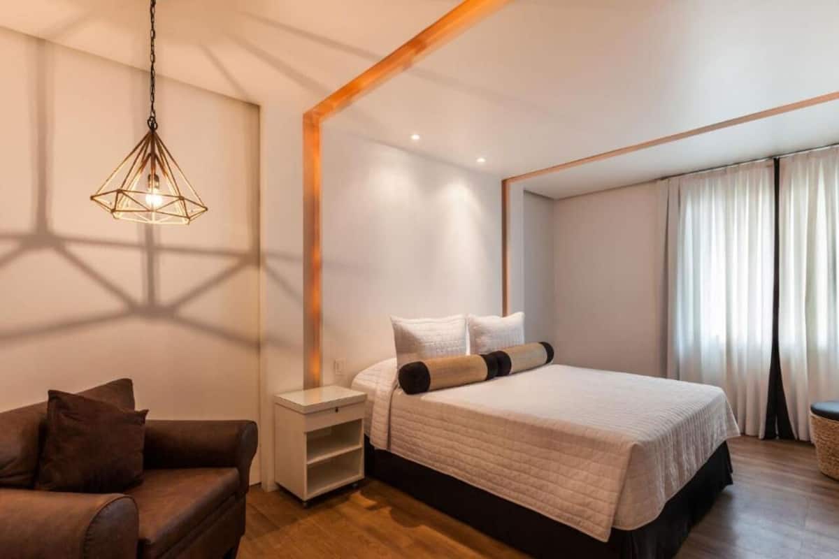 Une chambre à coucher moderne avec un lit, une table de chevet, un plancher en bois et un luminaire suspendu.
