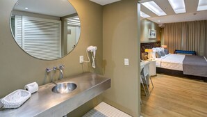A modern hotel room with a bathroom featuring a large mirror, two sinks, and a hairdryer. The room has a bed with a headboard, a desk, and a chair. - Rio Design Copacabana Hotel (Rio de Janeiro)