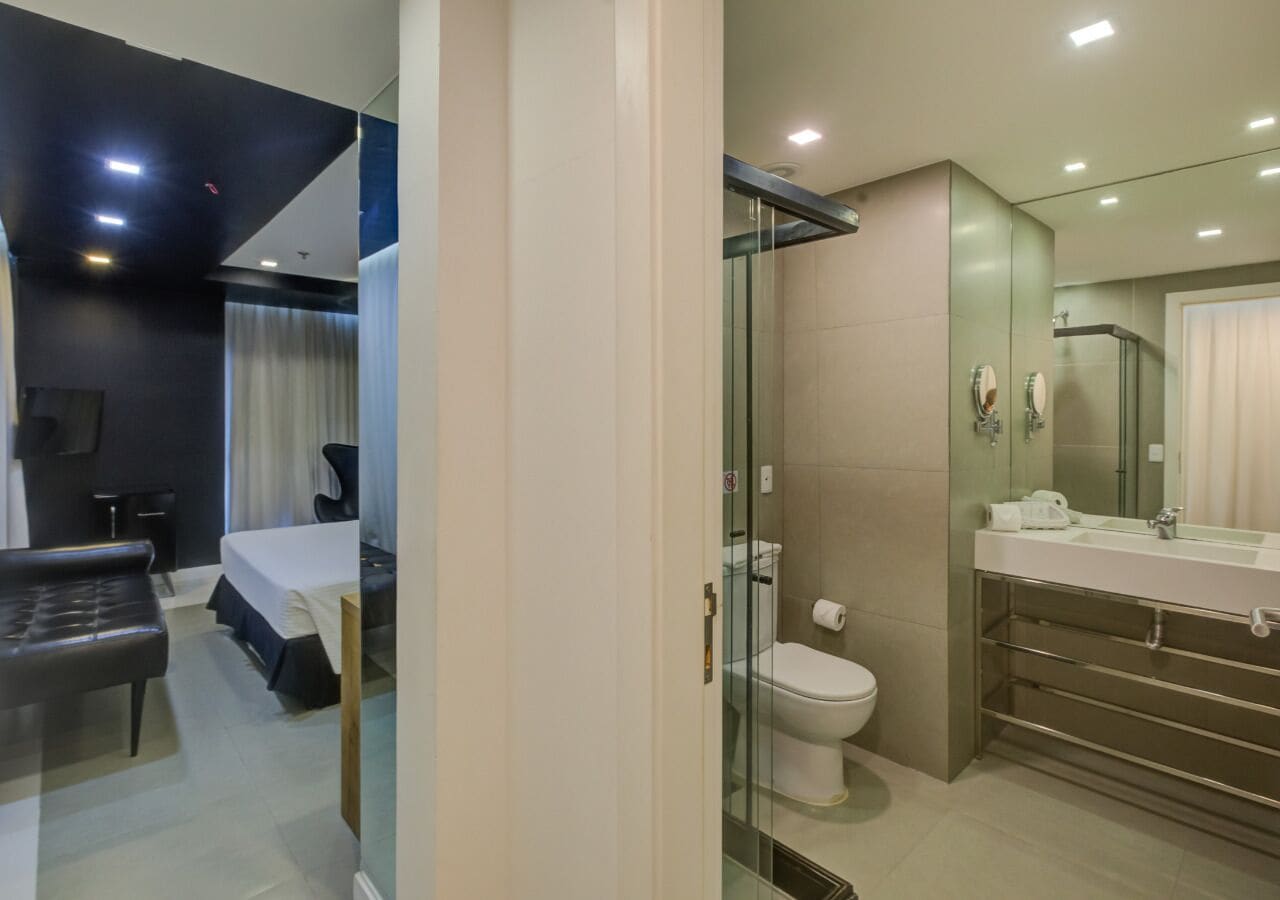 Une chambre d’hôtel moderne équipée d’un lit, d’un bureau et d’une douche séparée par des parois en verre.