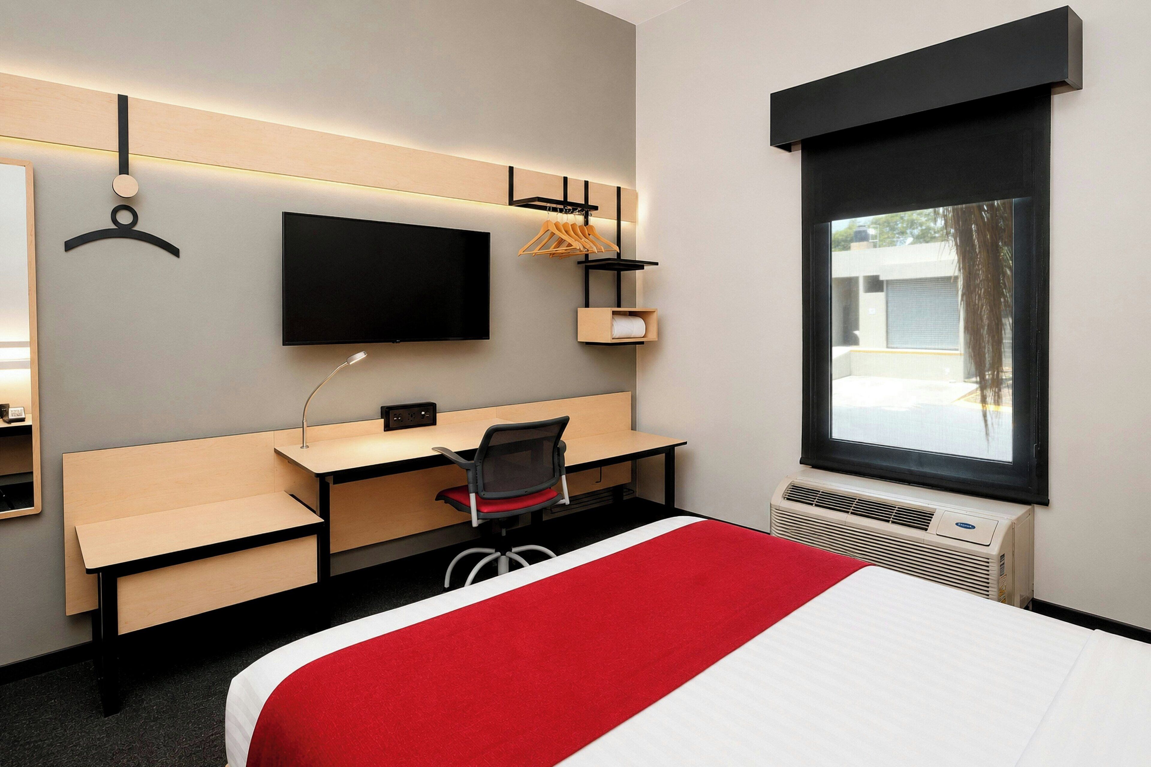 A hotel room with a bed, a desk, a chair, a television, and a window.