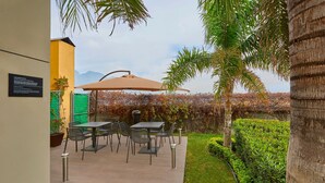 Un patio al aire libre con mesas y sillas, un espacio de estar cubierto y vistas a una cordillera.