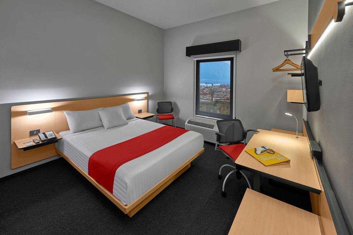 Een hotelkamer met een bed, nachtkastje, bureau, stoel en een raam met uitzicht.