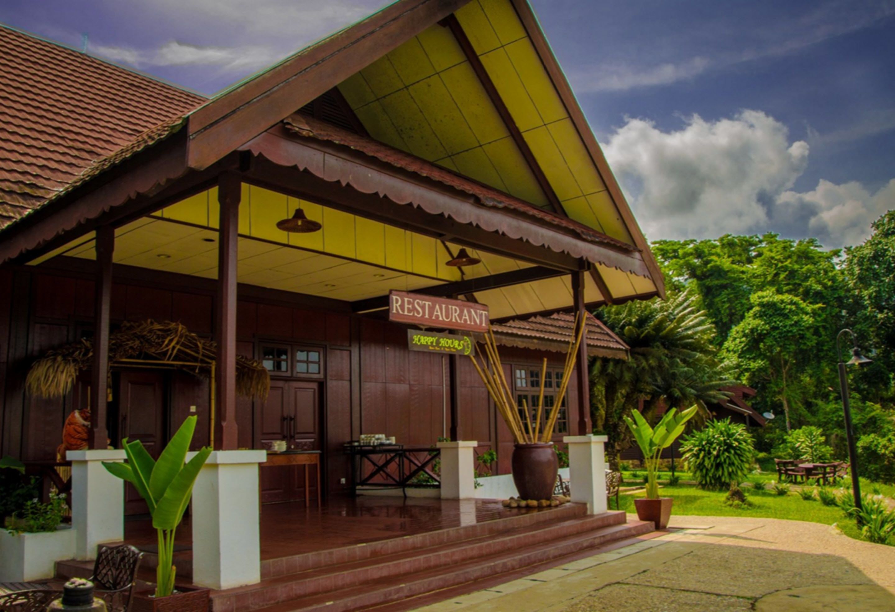 A restaurant with a covered patio, wooden exterior, and lush greenery in the background.