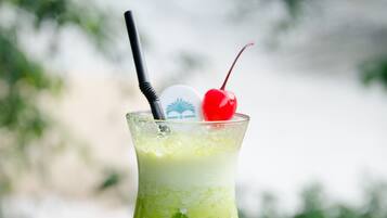 A tall glass with a green beverage, a straw, and a cherry on top, placed on a stone surface.