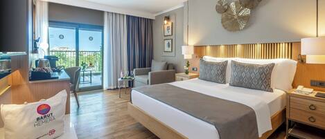 A hotel room with a bed, bedside tables, a desk, a chair, a balcony with curtains, and a view of the outdoors.