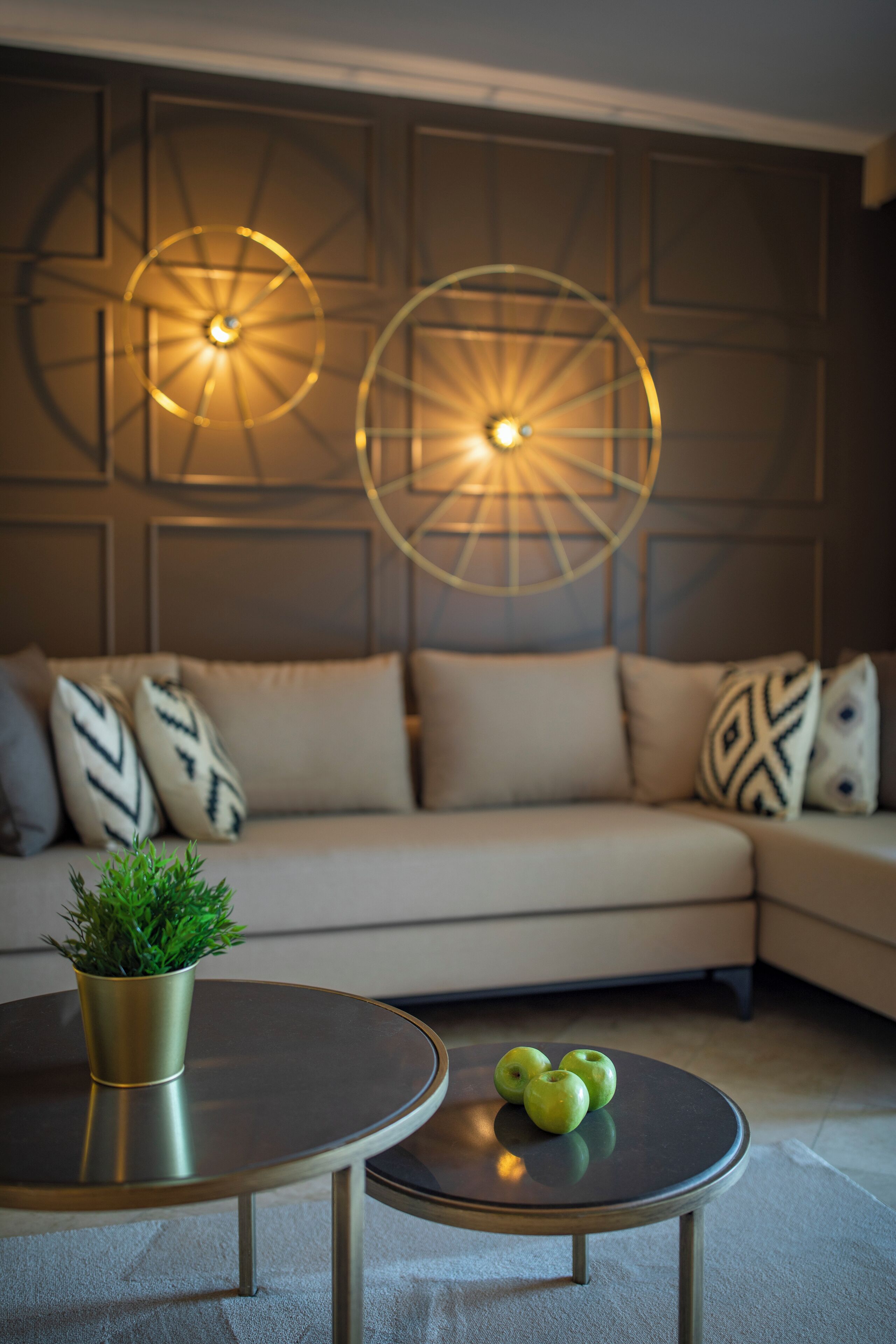 Un salon moderne avec un canapé d’angle, deux tables rondes et des panneaux décoratifs muraux.