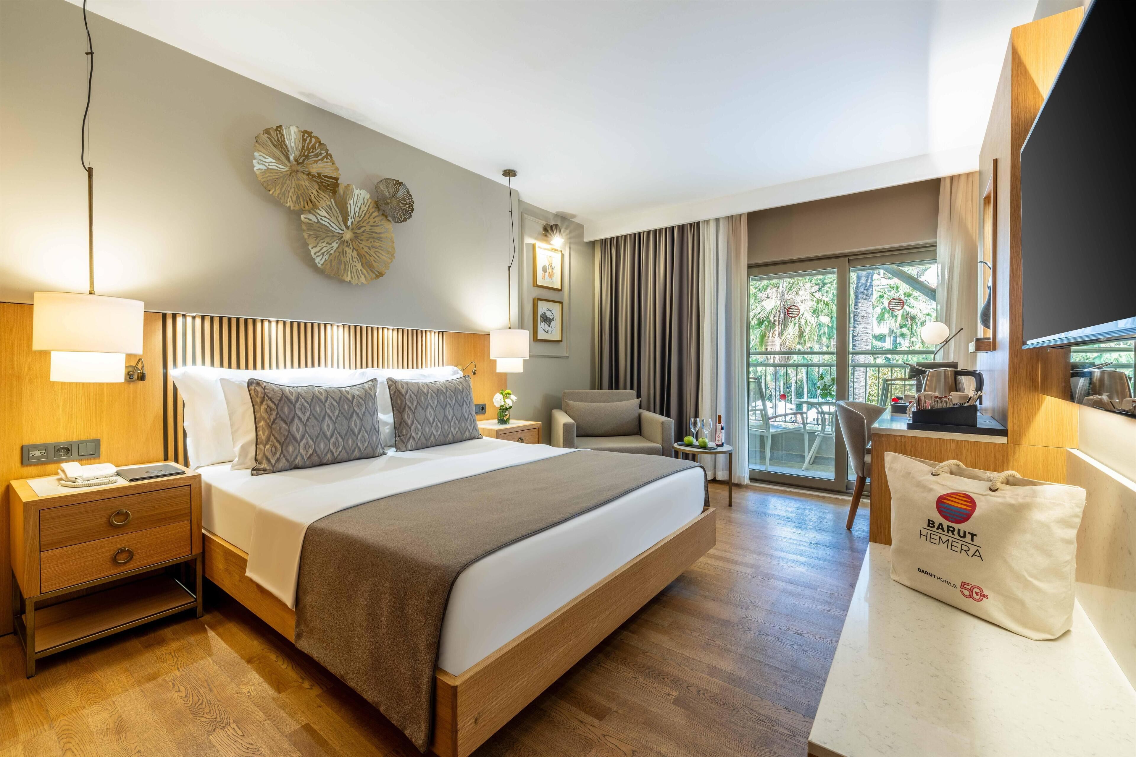 A hotel room with a large bed, a bedside table with a lamp, a chair, a TV, and a view of the outdoors.