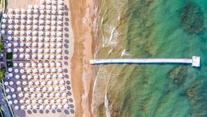 Une vue aérienne d’une plage, avec des rangées de parasols et une longue jetée qui s’avance dans l’eau.