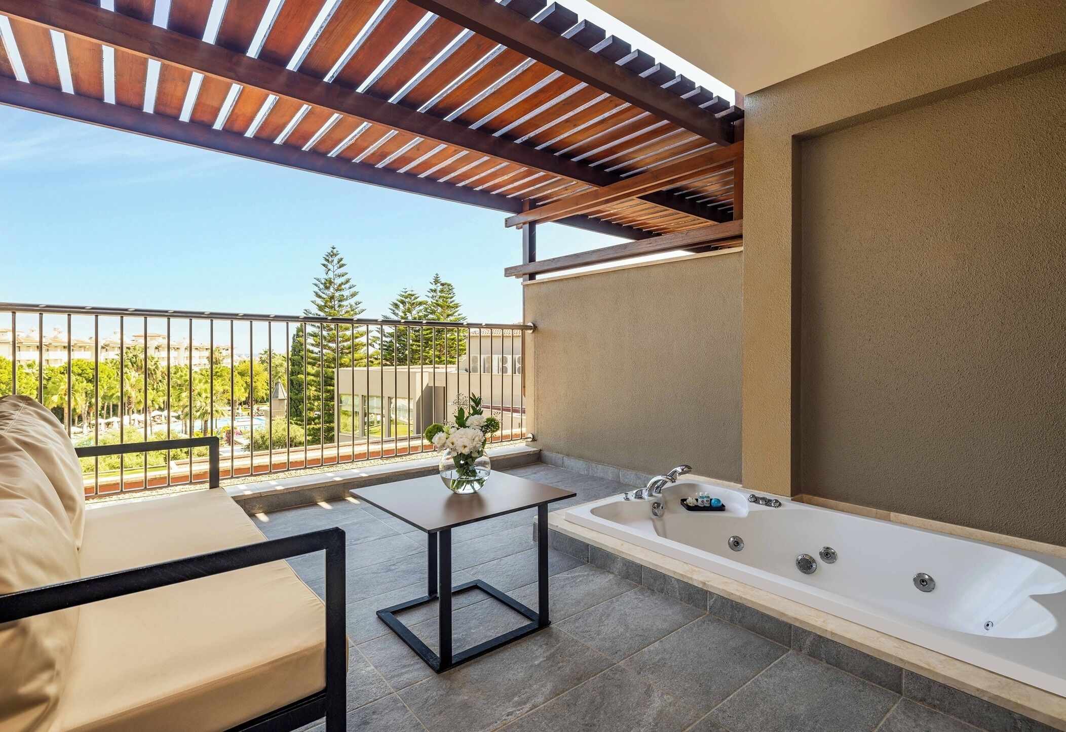 A balcony with a sofa, a small table with a vase, and a bathtub.