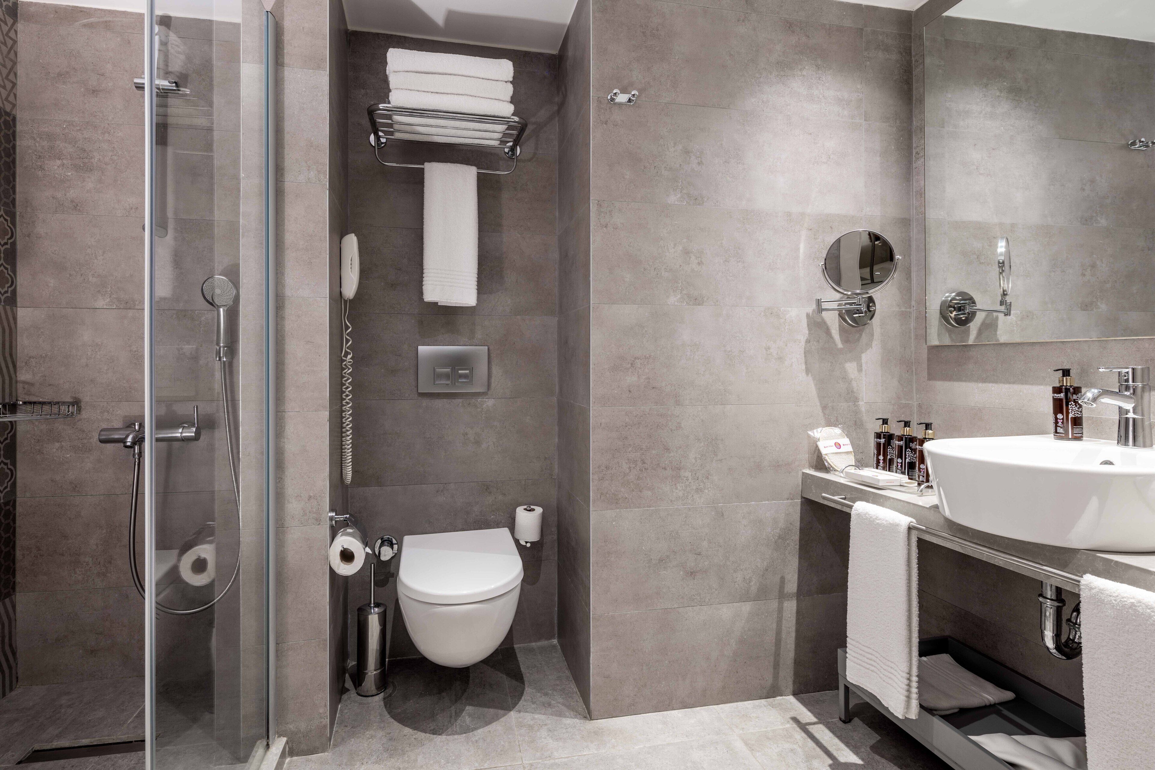 Un baño moderno con cabina de ducha de vidrio, inodoro, lavamanos con espejo y toallero.