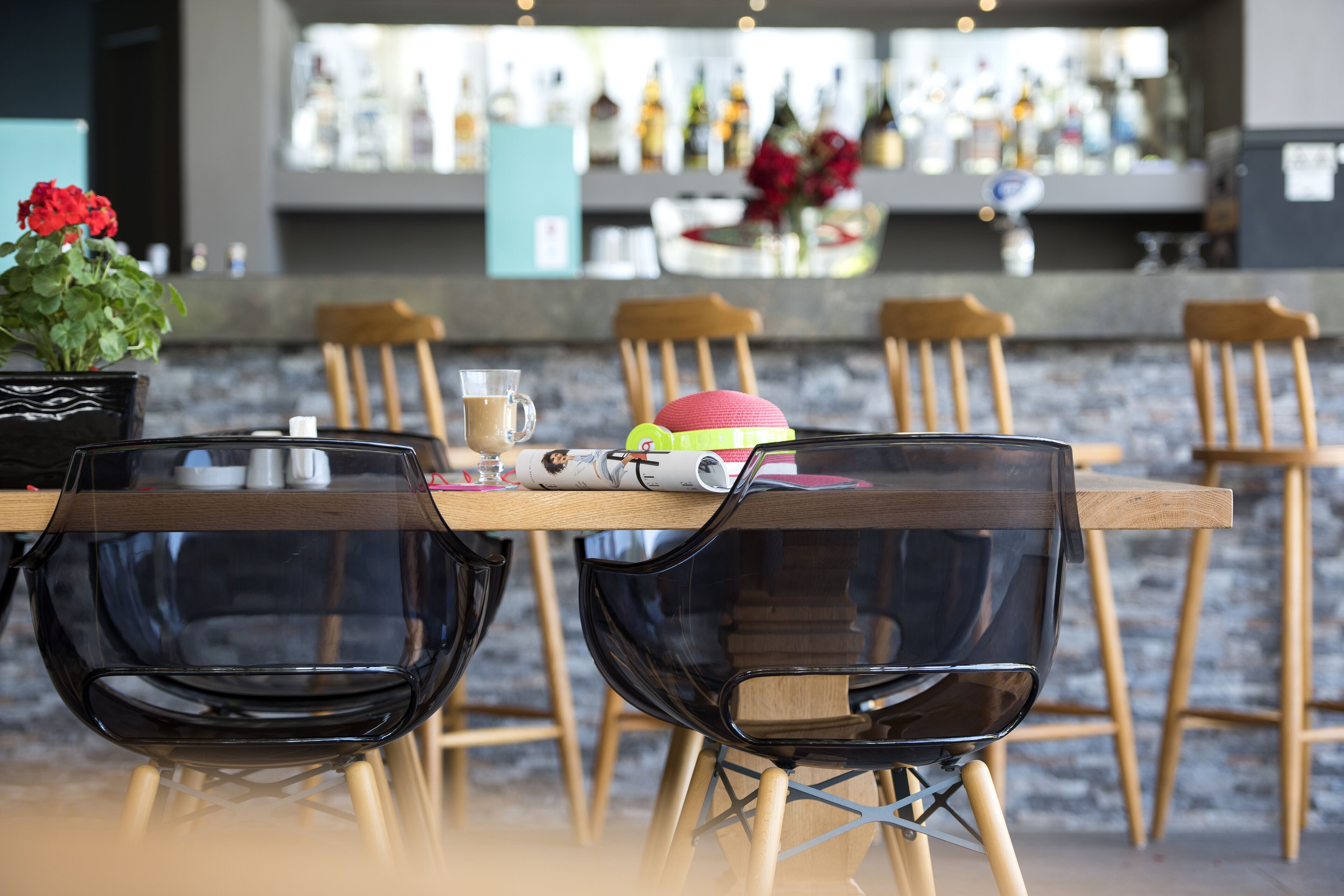 A dining area with a wooden table, black chairs, a glass table, and a bar in the background.