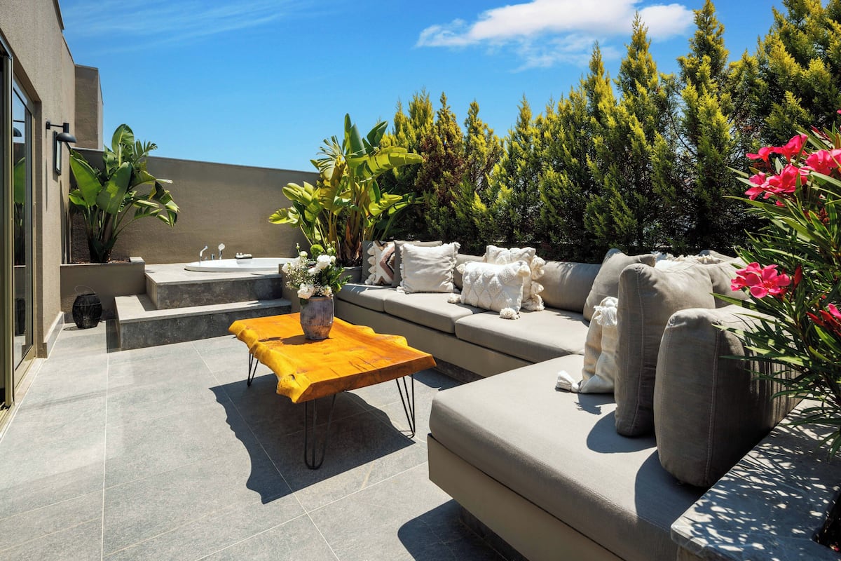 A modern outdoor seating area with a sofa, a wooden coffee table, and a planter with flowers.