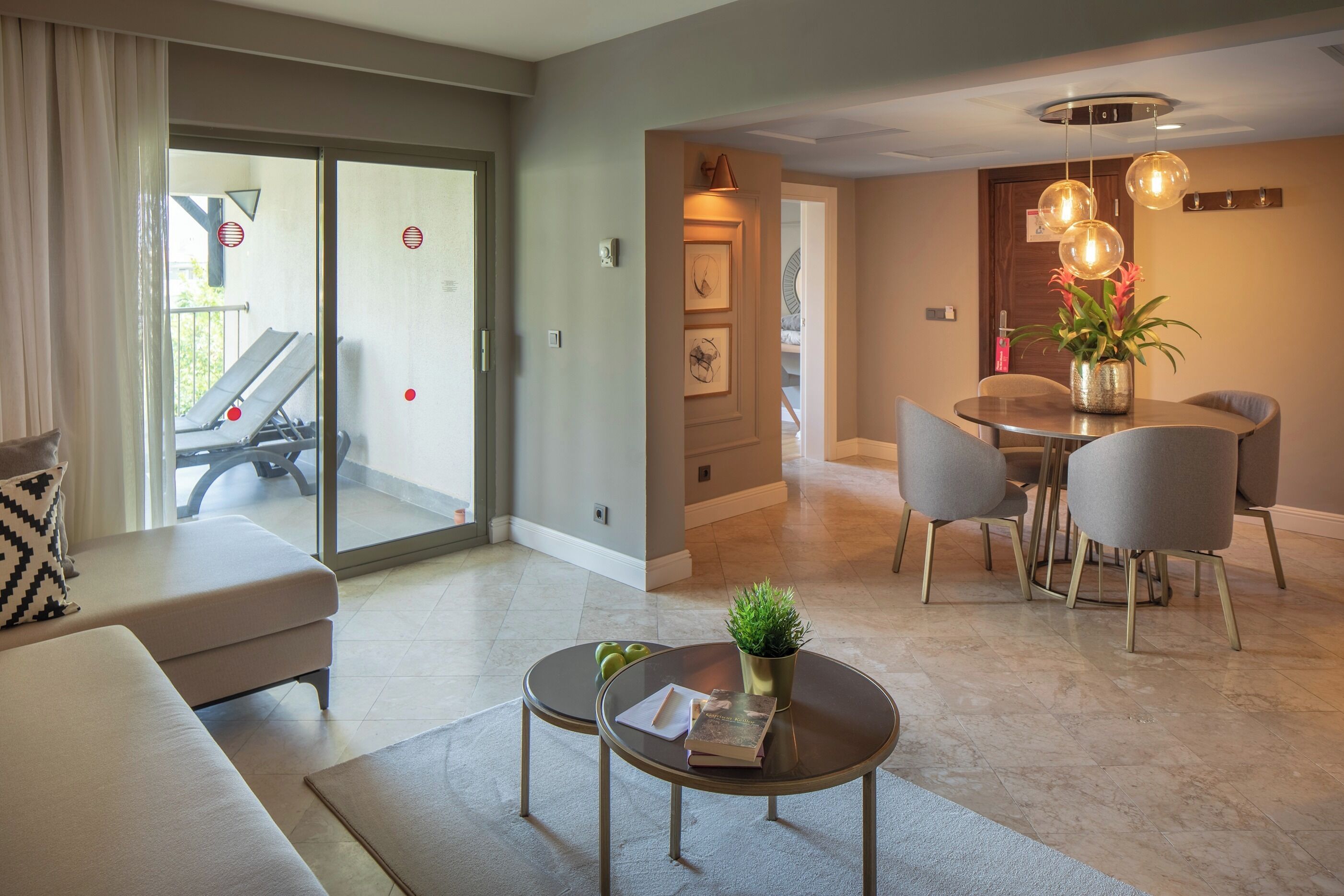 A modern living room with a sofa, two coffee tables, a dining area with a table and chairs, and a sliding glass door leading to a balcony.