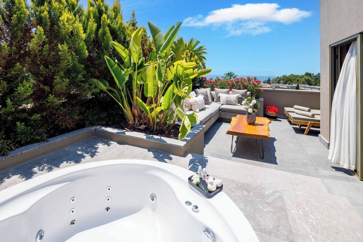 A rooftop terrace with a hot tub, seating area, and lush greenery.